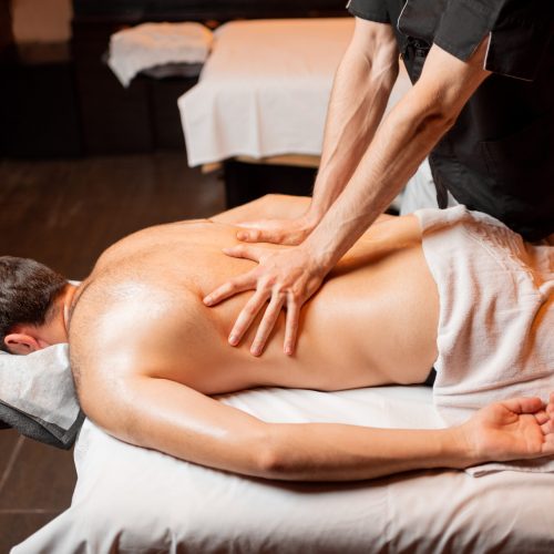 Man receiving a deep massage on his back from professional therapist at luxury spa salon