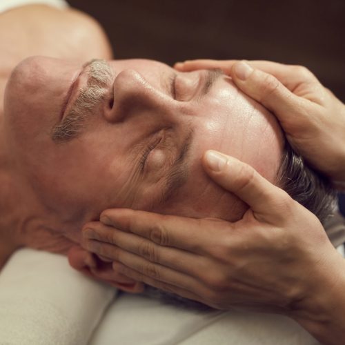 High angle close up of handsome senior man enjoying facial massage at luxury SPA center, copy space